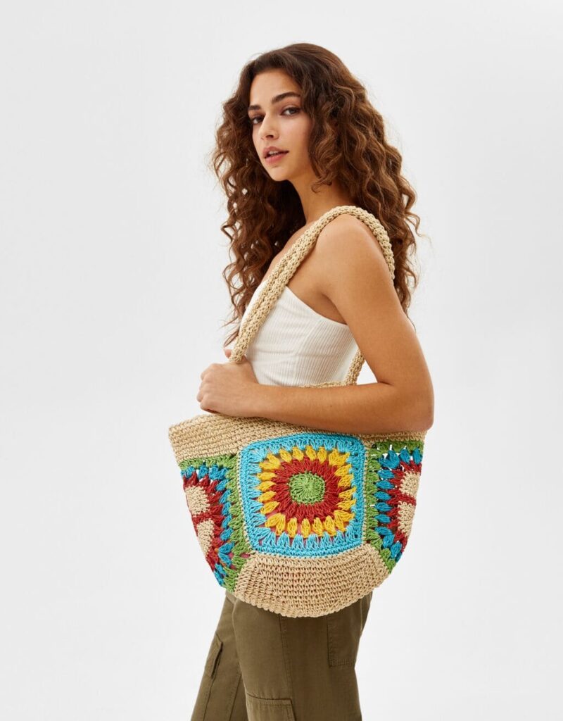 modella in piedi di fianco con canotta bianca e borsa mare colorata a fiori bershka