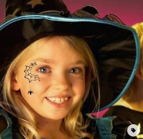 bambina sorridente con cappello da strega e trucco da strega, con disegno di ragnatela sul viso 