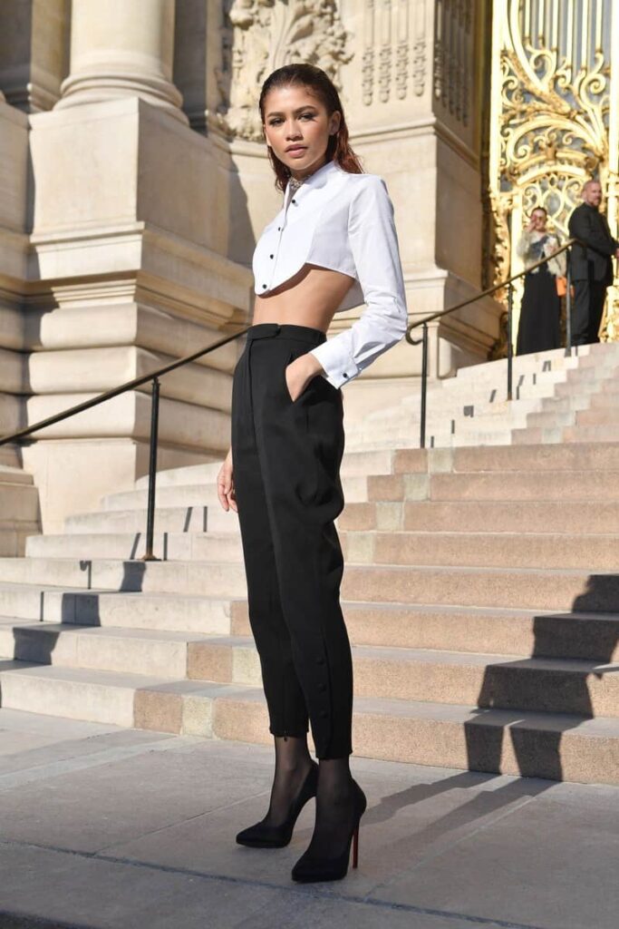Zendaya indossa pantalone nero e camicia crop bianca con scarpa decollete nera 