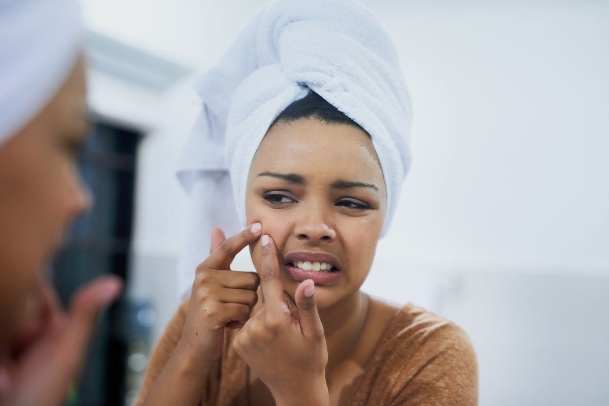 ragazza con turbante in testa davanti lo specchio che si tocca un brufolo
