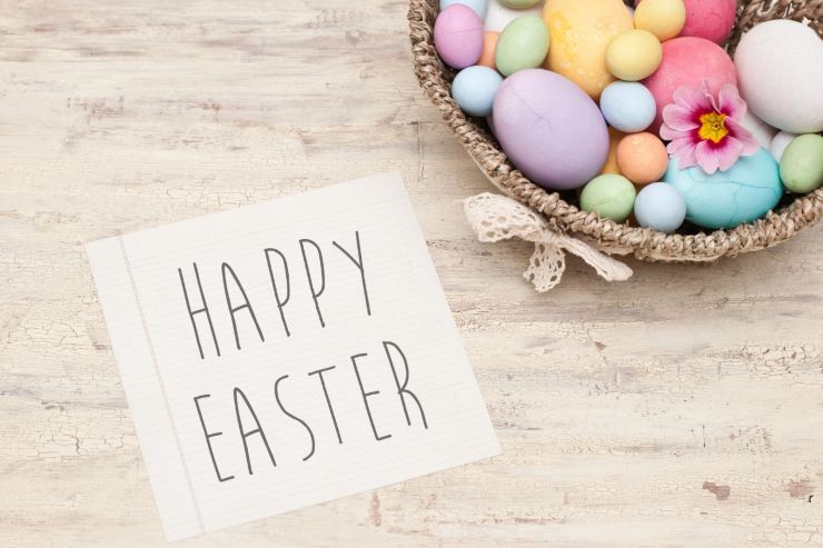 uova colorate in un cesto e foglio con scritto "happy easter"