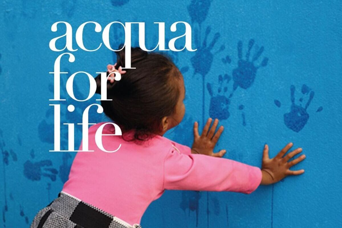 bambina di colore con maglia rosa che stampa le impronte delle mani su un muro blu, progetto acqua for life giorgio armani