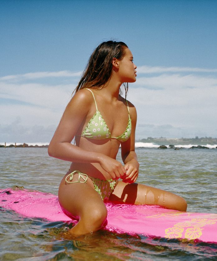 modella seduta su surf in mezzo al mare mentre indossa costume pull&bear verde chiaro