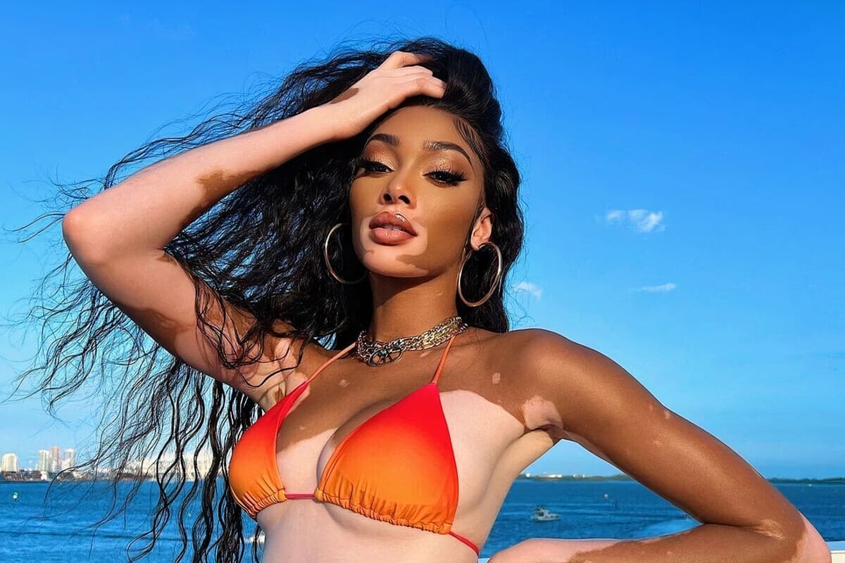 winnie harlow posa in bikini arancione e capelli lunghi scuri e mossi al vento e sfondo mare
