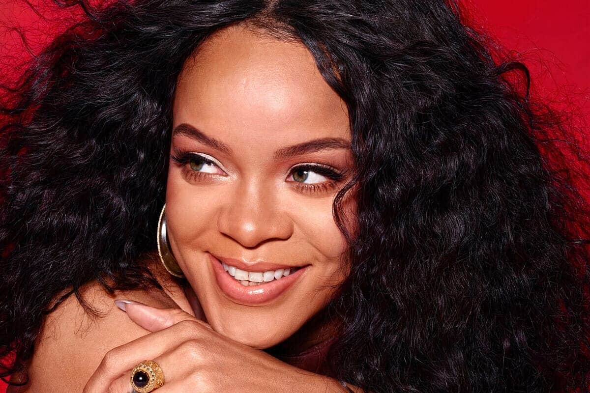 primo piano Rihanna con capelli ricci e pelle luminosa su sfondo rosso