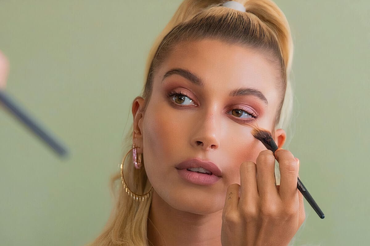 Hailey Bieber si trucca su sfondo verde pastello - i migliori prodotti make-up di Agosto