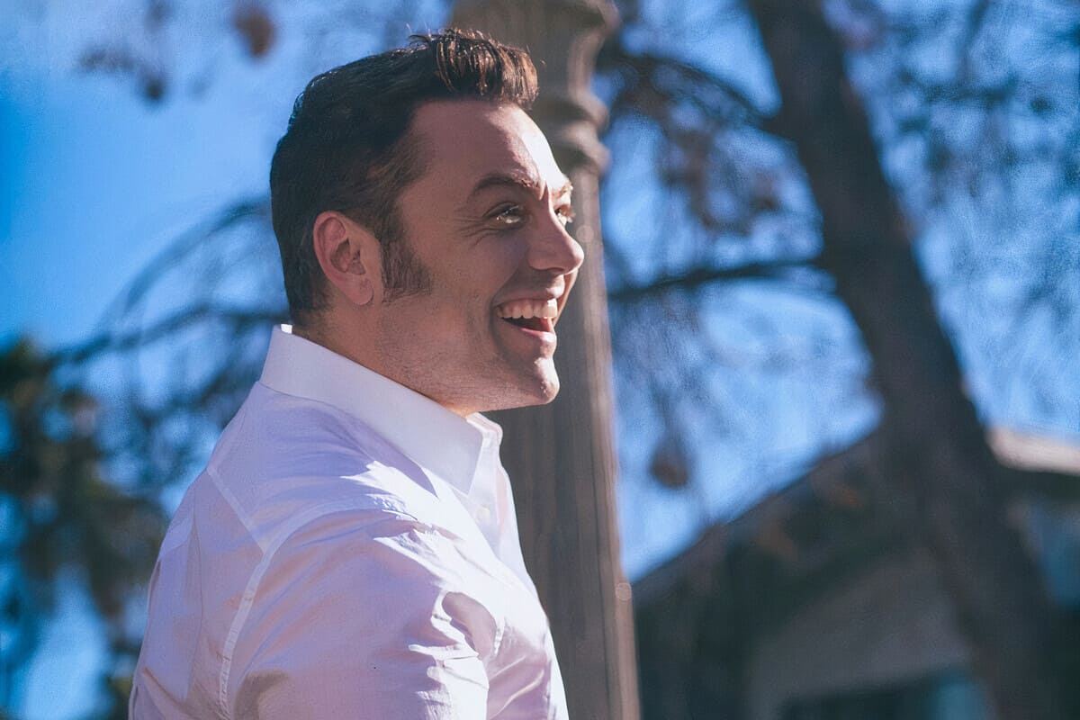 Tiziano Ferro di profilo sorridente in un parco