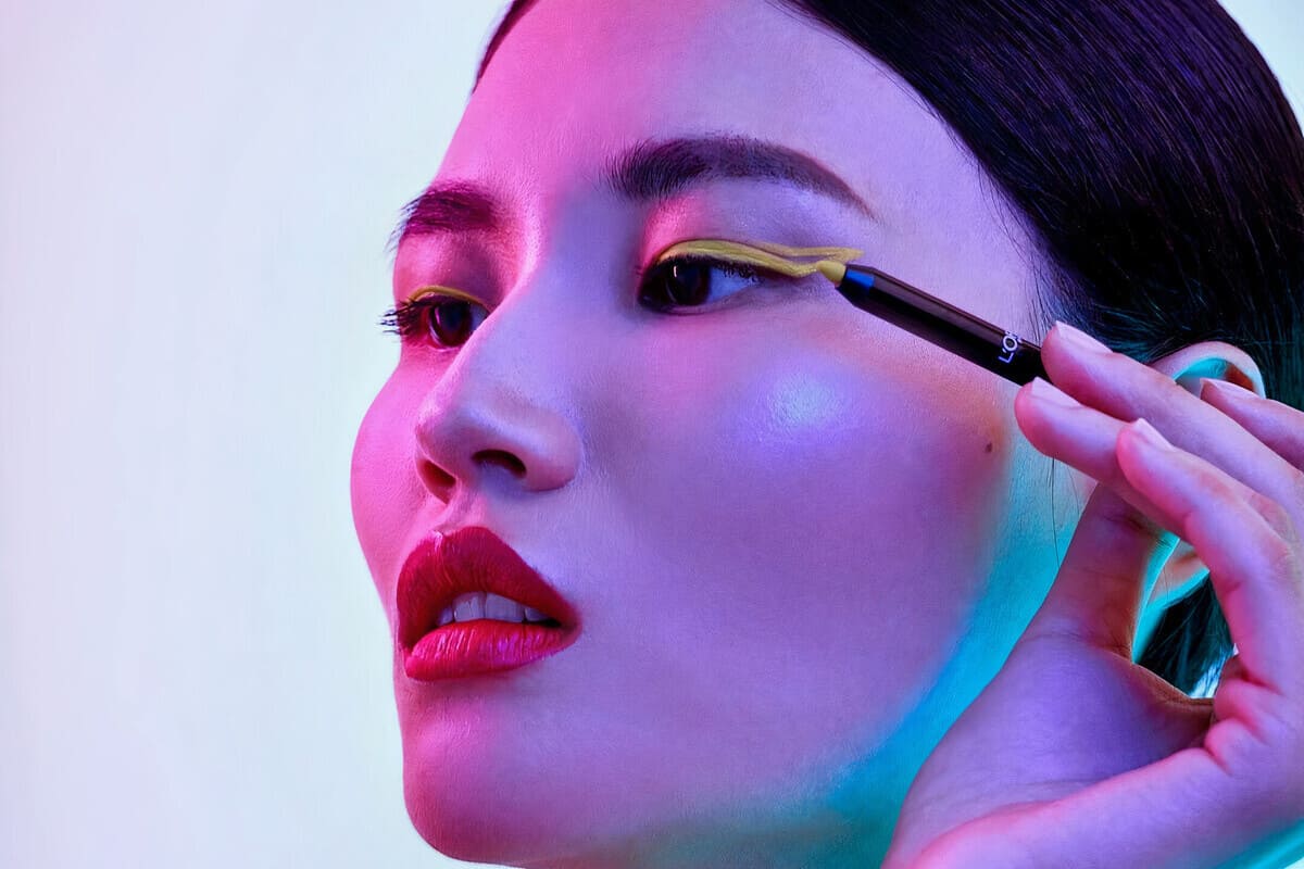 modella con occhi neri che si trucca con matite colorate