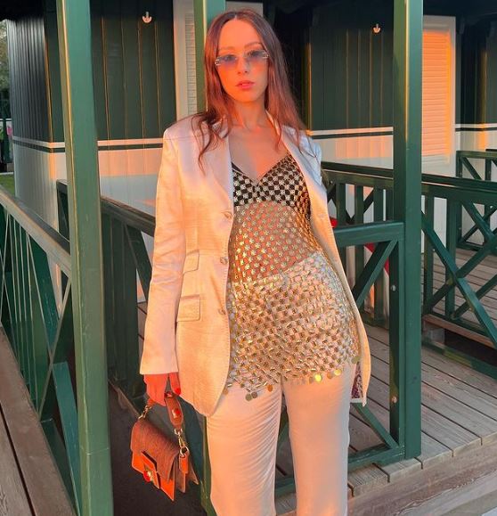 ragazza con completo giacca e pantalone di colore bianco e top paillettes trasparente con in mano una mini bag arancione