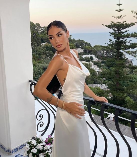 ragazza in posa con abito in seta bianco, capelli raccolti, con vista sul mare