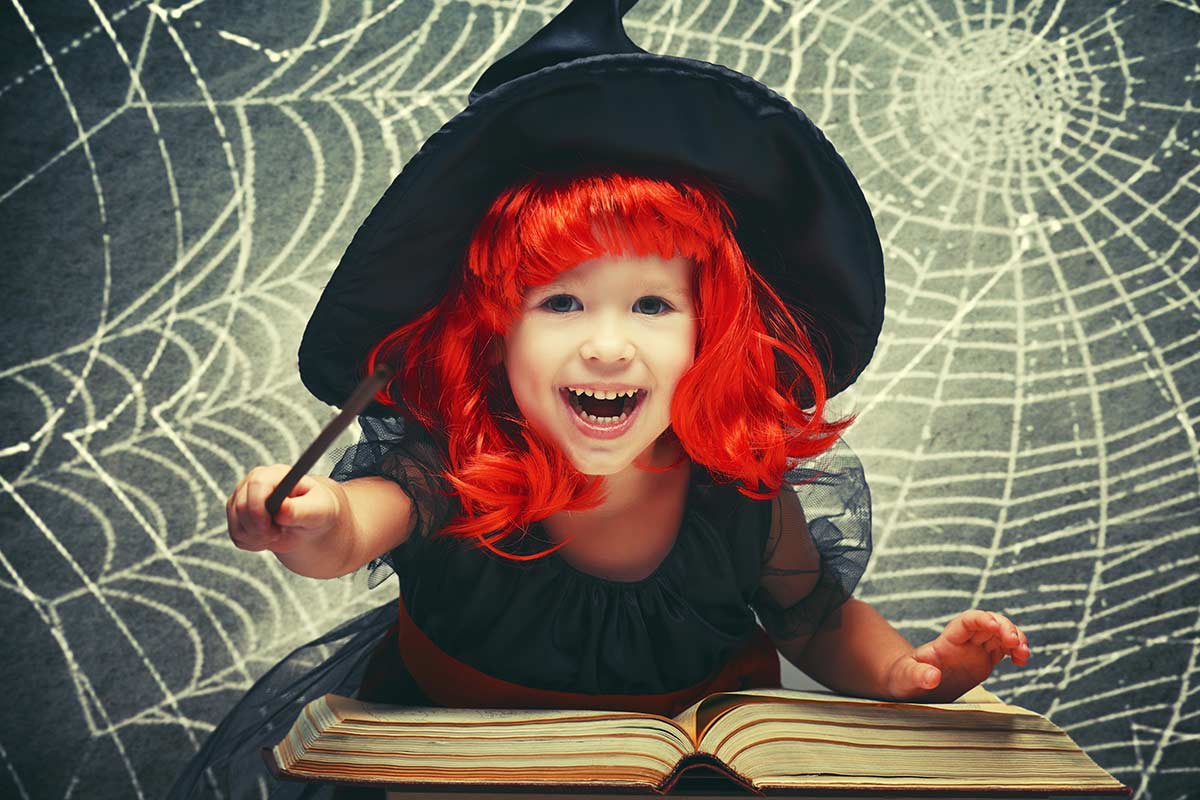 Bambina con capelli rossi vestita da streghetta che legge un libro per Hallowen