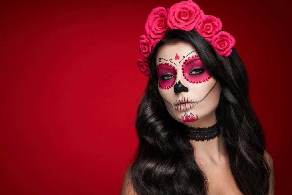 ragazza con makeup da scheletro nei colori bianco, nero e rosa, con capelli neri e rose fucsia in testa