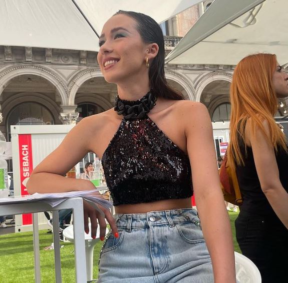 ragazza sorridente indossa top nero con pailletes e jeans azzurro chiaro seduta ad un tavolo