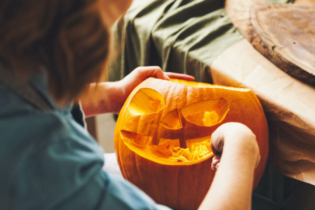 mani di ragazza che intagliano con coltello una zucca, incidendo bocca ,mani e naso