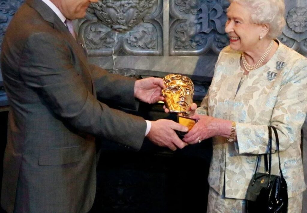 La regina Elisabetta riceve un premio con la borsetta alla sua sinistra