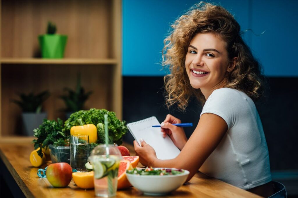 Ragazza sorridente, a tavola con verdure e frutta, mentre controlla la sua dieta