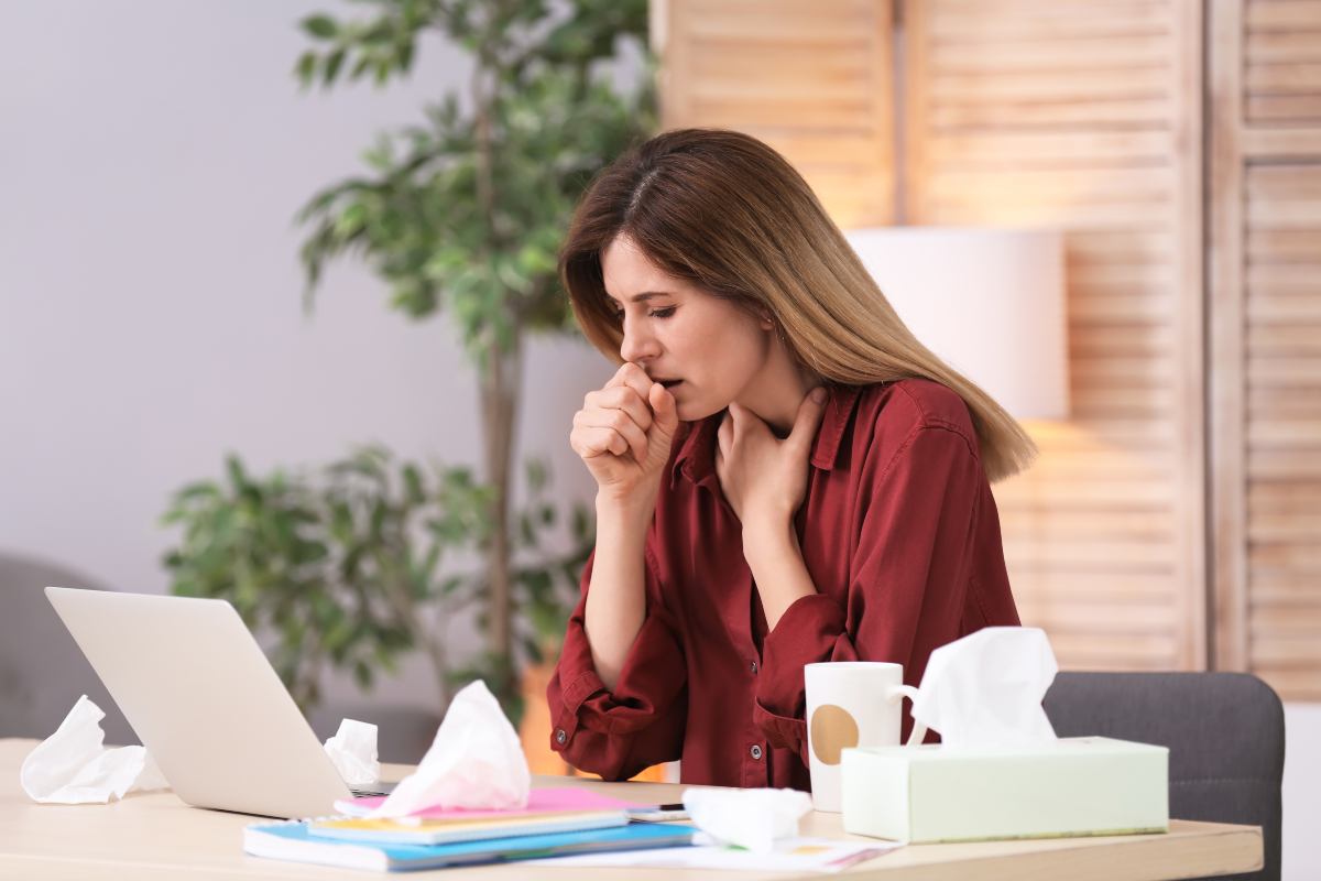Donna in ufficio davanti ad un laptop, con camicia bordeaux, che tossisce