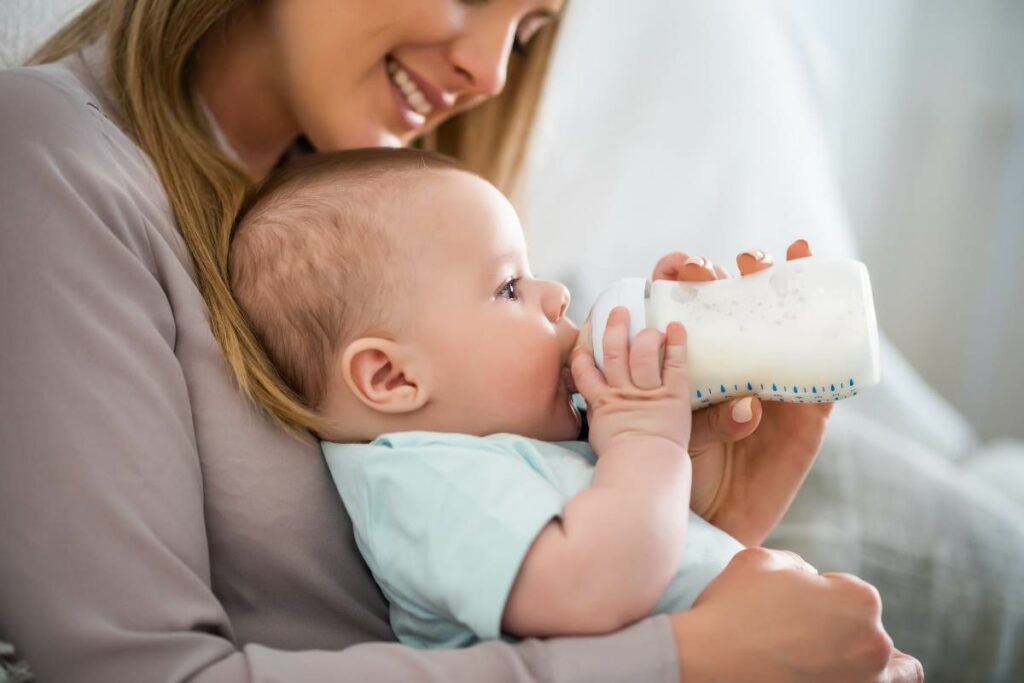 Madre con il neonato sulle ginocchia mentre beve da solo il suo biberon