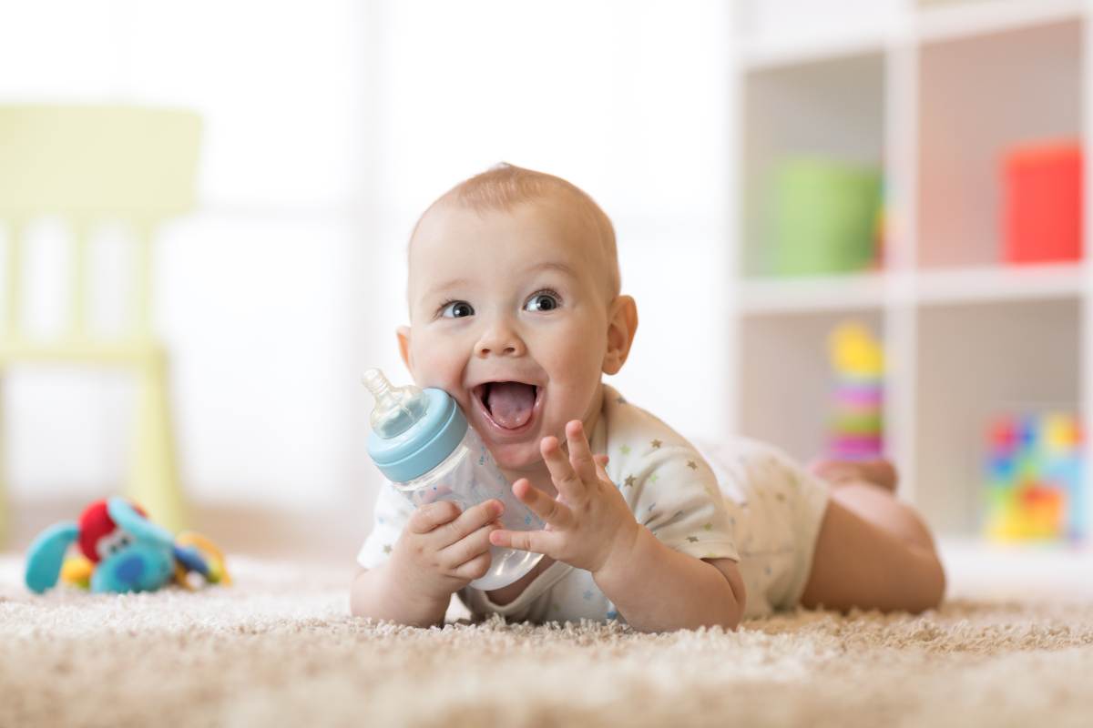 Bambino con biberon sorridente e sul tappeto