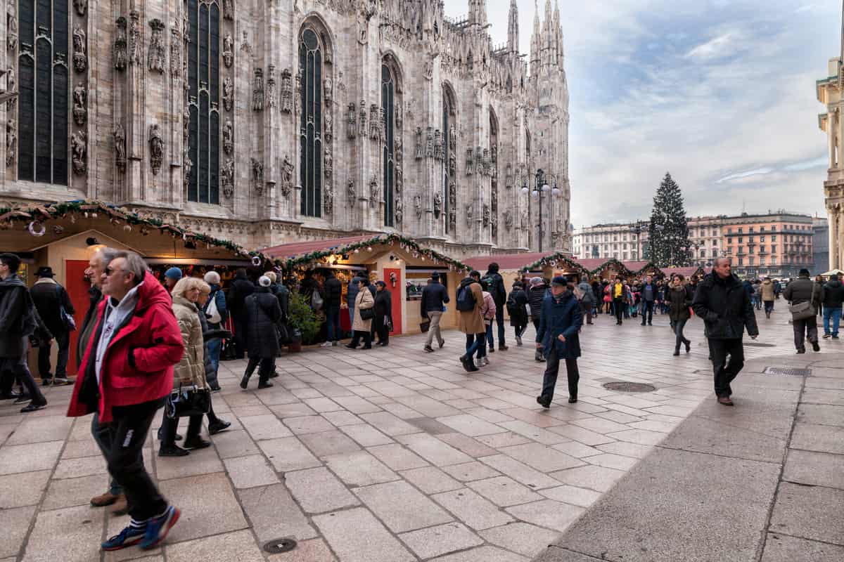 piazza Duomo a Milano con mercatini di Natale, casottini in legno e persone che passeggiano