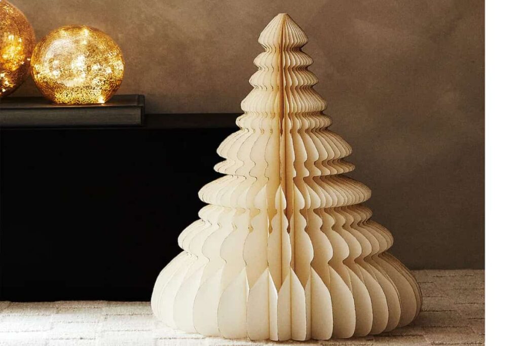 albero di natale di colore bianco in carta origami, sullo sfondo due lampade natalizie di colore oro