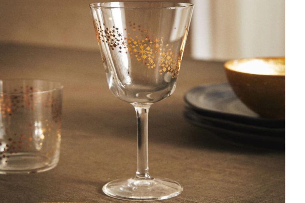 calice da vino a tema natalizio con stelline dorate e in secondo piano bicchiere da acqua con lo stesso tema