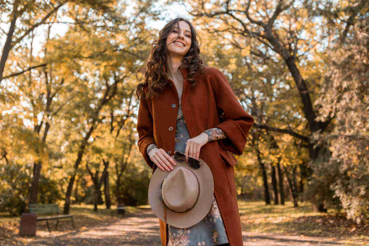 donna con cappotto ruggine e cappello in mano