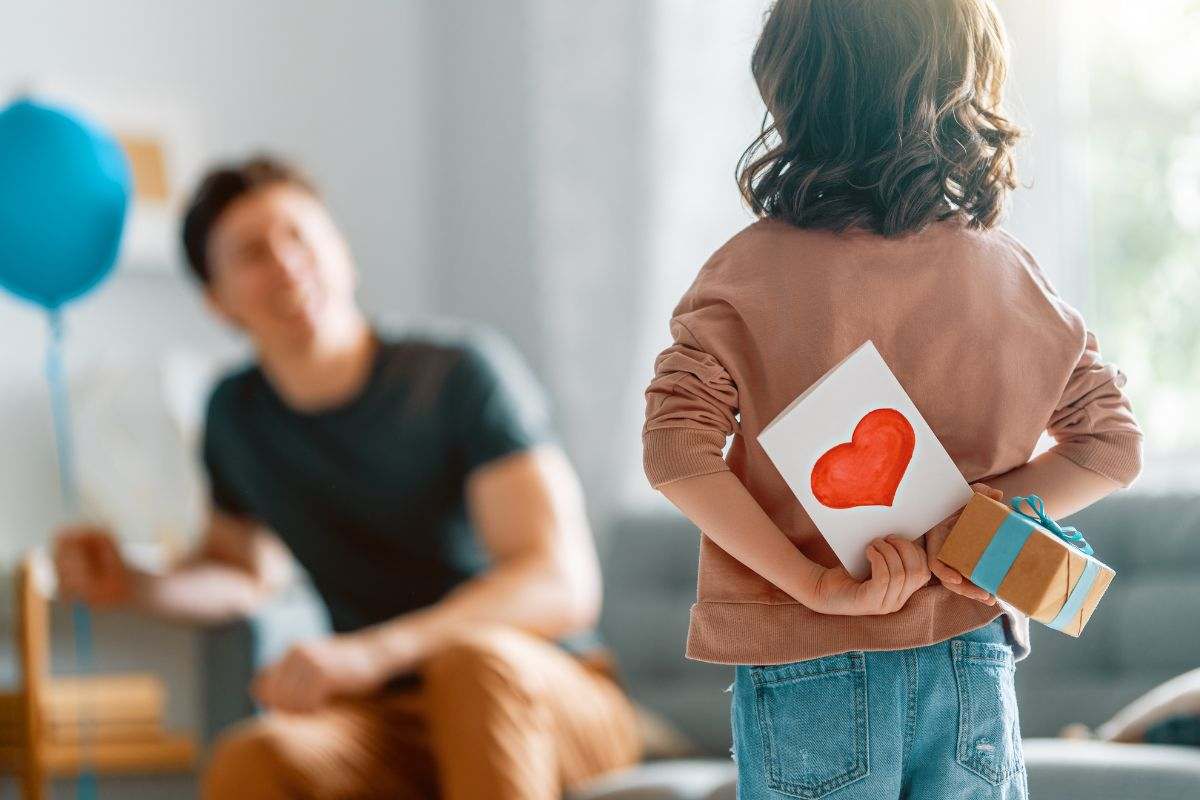 bambino con un biglietto e un regalo nascosti dietro la schiena che guarda il papà
