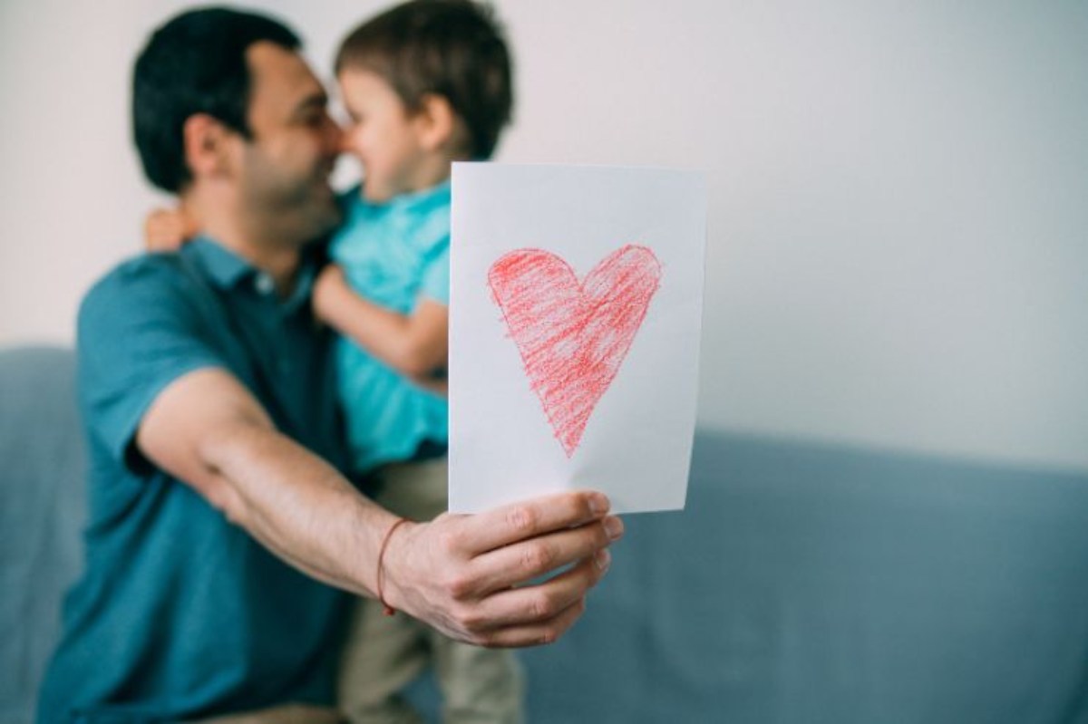 bimbo che abbraccia il papà con cuore disegnato su un foglio bianco