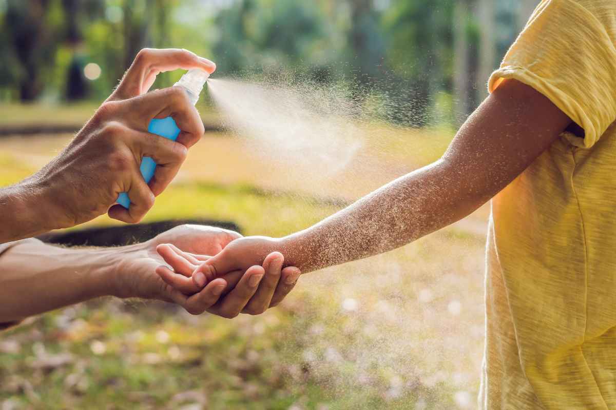 Mamma che spruzza spray antizanzare sul braccio del figlio