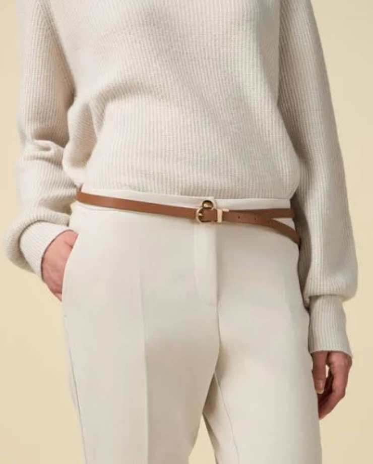 donna con maglione bianco a costine, pantaloni bianchi e cintura sottile marrone