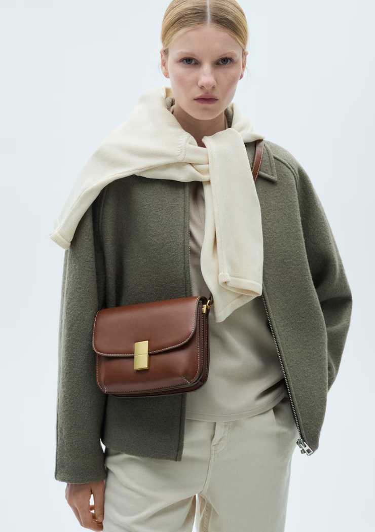 modella con giacca verde, maglia bianca sulle spalle, felpa e pantaloni bianchi e borsa a tracolla marrone