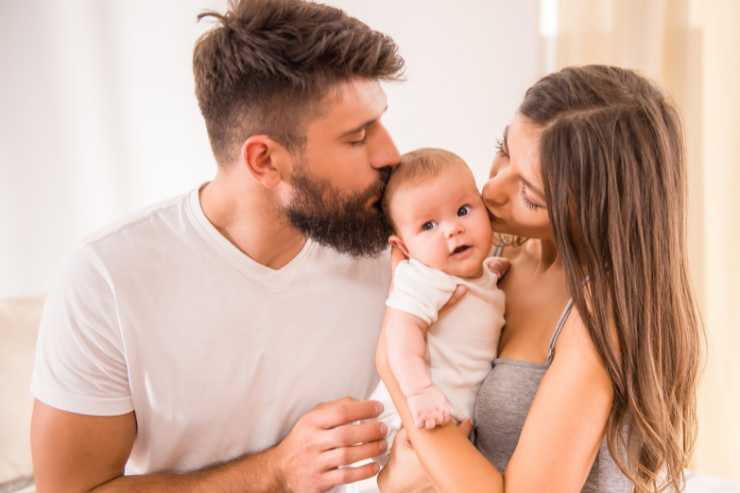 coppia di genitori che baciano un neonato