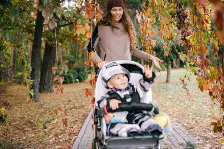 mamma con bambino sul passeggino in un parco autunnale