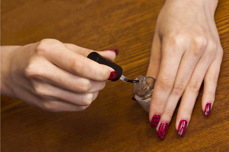 mani che applicano top coat trasparente su smalto roso
