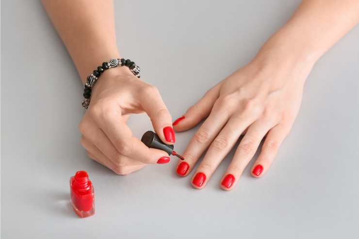 donna che applica smalto rosso sulle unghie