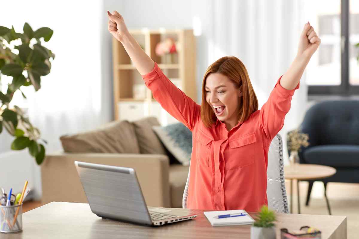 donna felice davanti al computer con braccia alzate in segno di vittoria