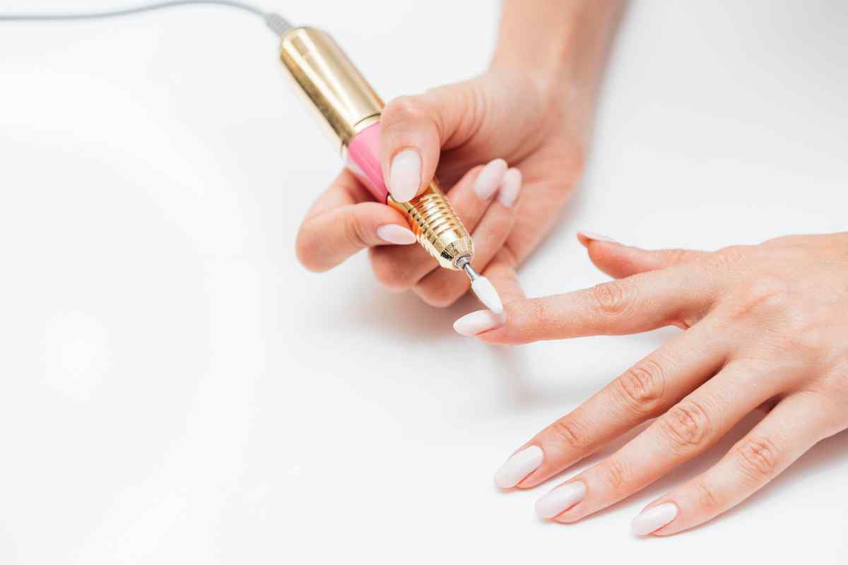primo piano mani donna che usa fresa elettrica per unghie