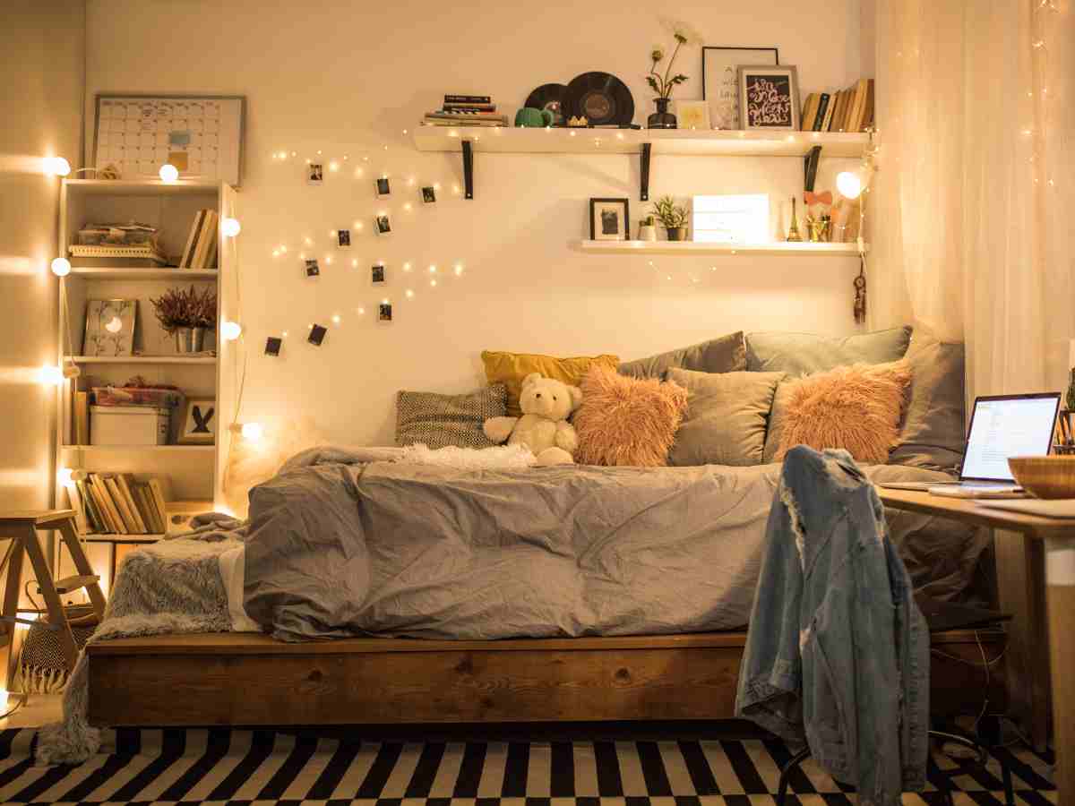stanza in affitto con luci led, mensole, libreria e cuscini sul letto