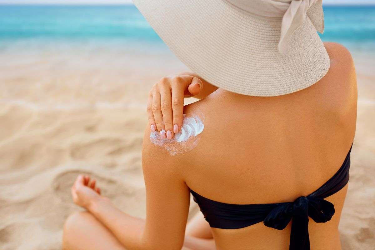 ragazza che spalma crema al mare sulla spalla