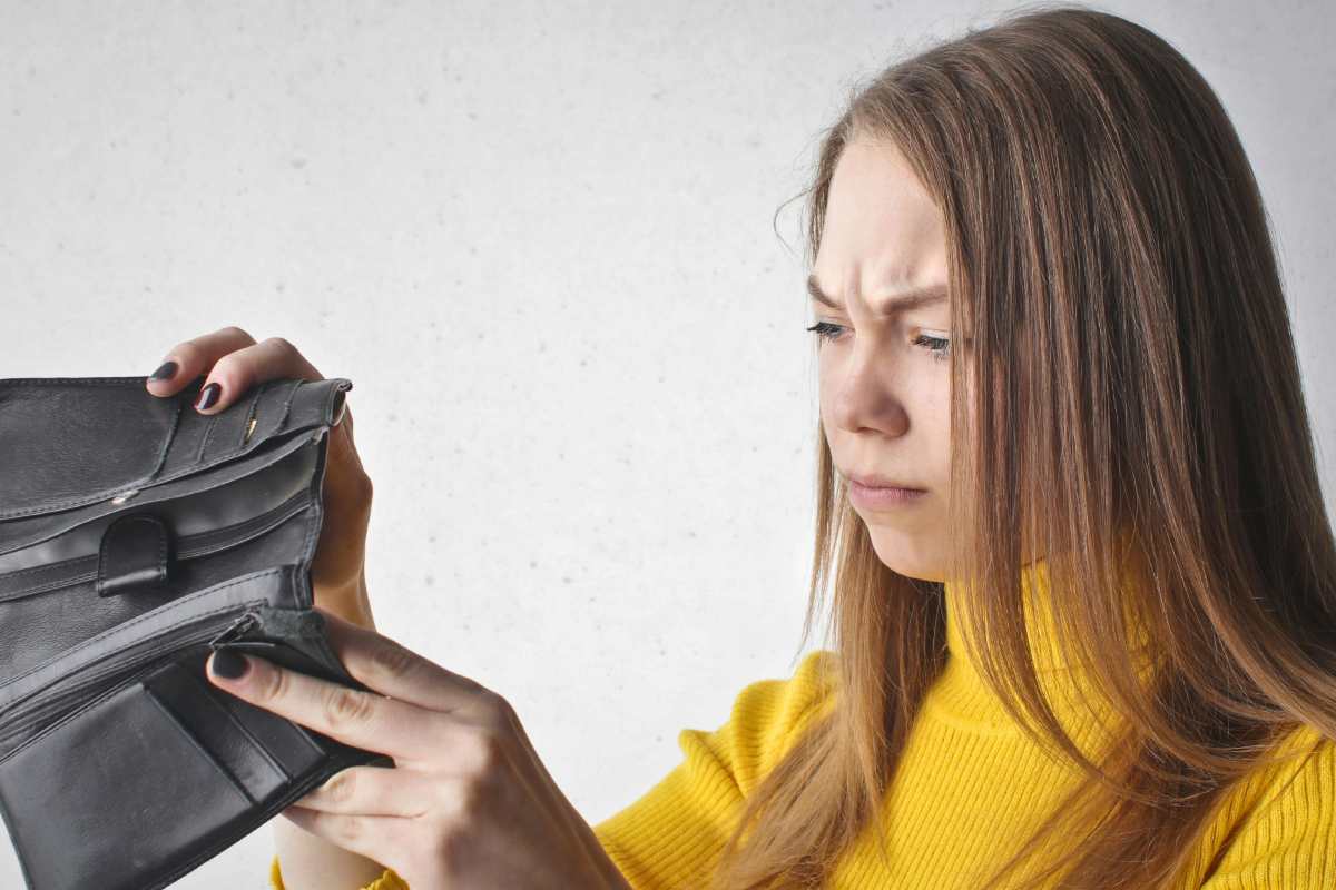 Ragazza con maglione giallo che guarda in un portagogli vuoto