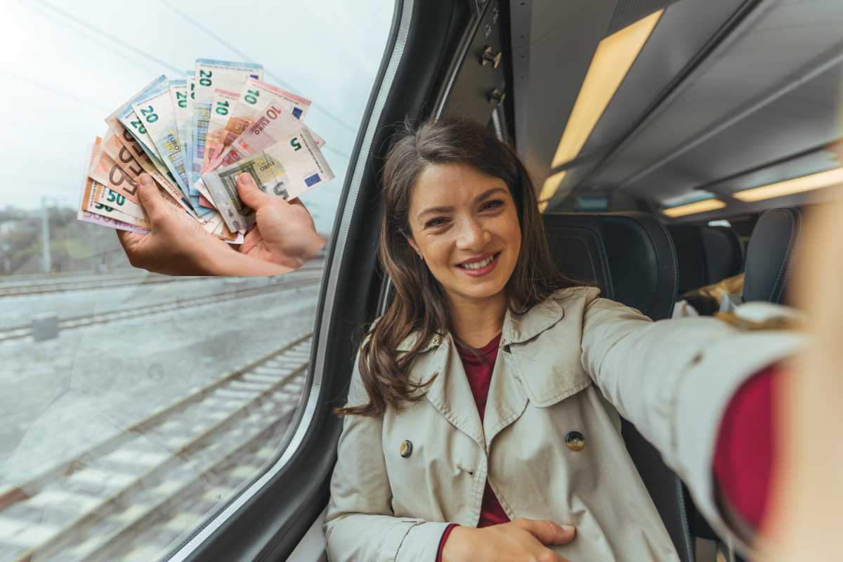 donna su un treno si scatta un selfie, vicino banconote simbolo del bonus trasporti