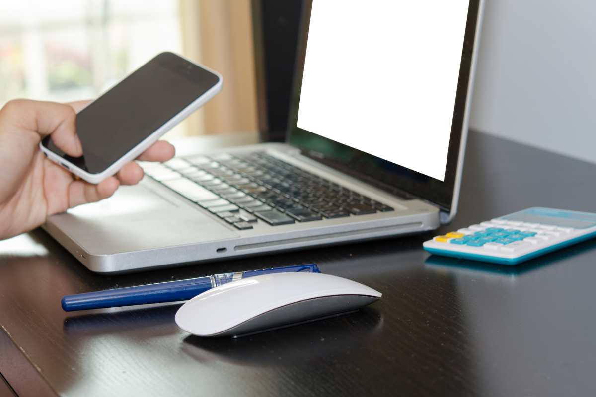 smartphone in mano e laptop sulla scrivania per spiare il cellulare dal pc