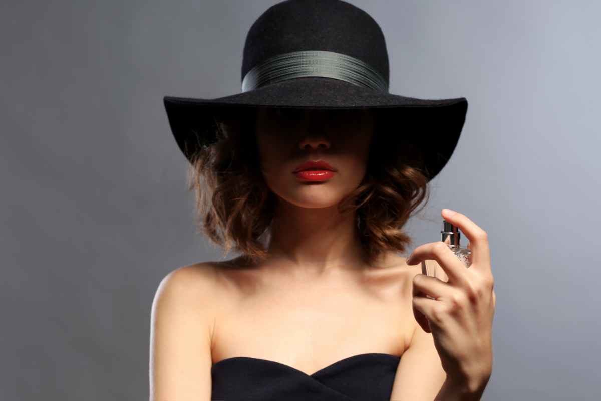 donna con cappello che copre il viso si spruzza un profumo