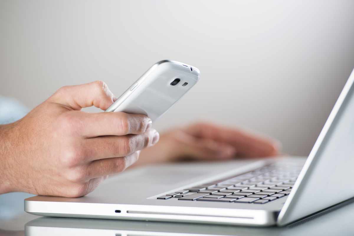 uomo con smarthphone in mano e pc portatile aperto