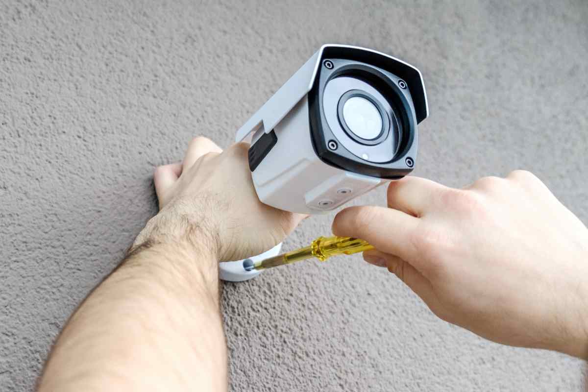 mani avvitano una telecamera sul muro
