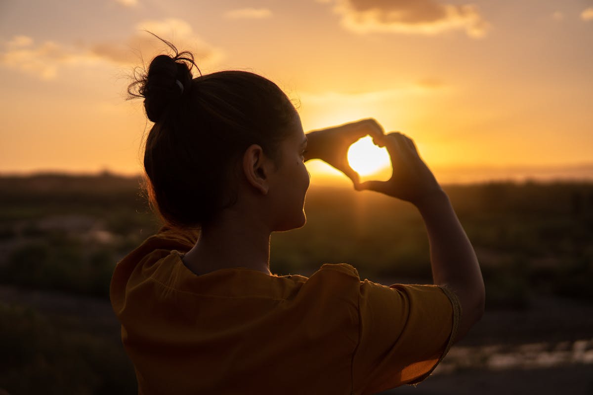 donna con chignon messy che fa cuore al tramonto