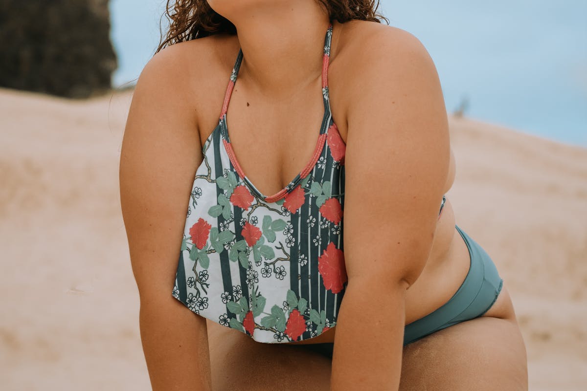 donna curvy in costume e in ginocchio sulla spiaggia