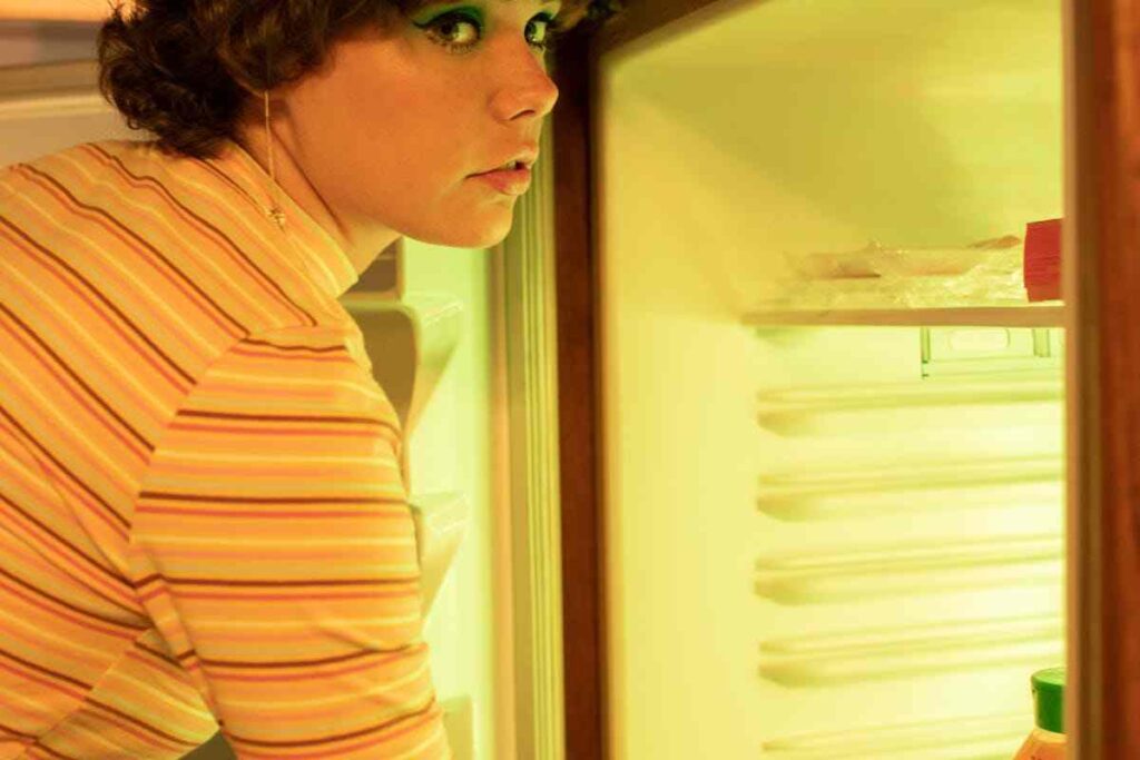 donna truccata davanti allo scompartimento del frigorifero aperto