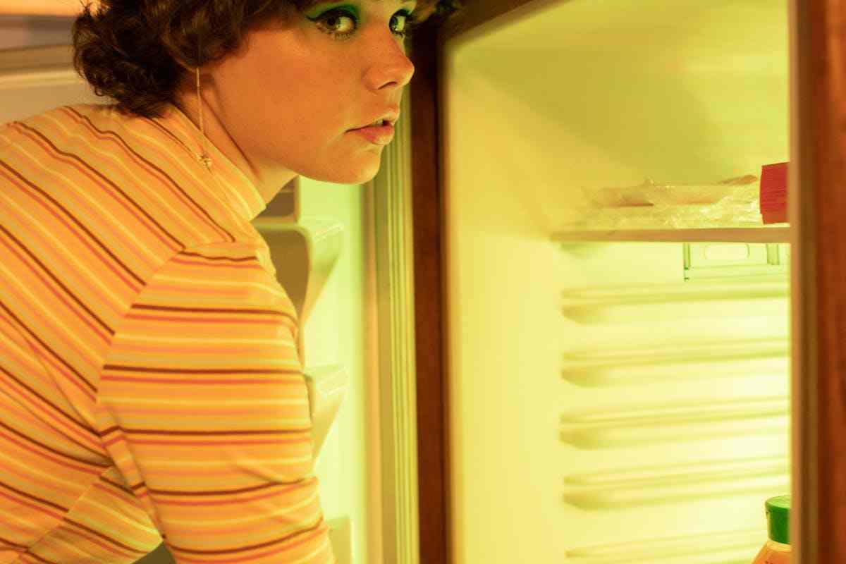 donna truccata davanti allo scompartimento del frigorifero aperto
